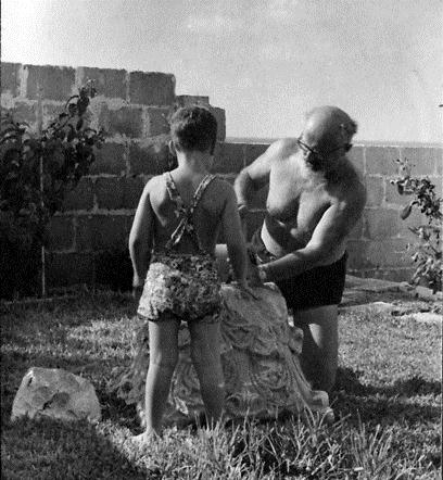 יצחק עם בנו בגן ביתם, חוצב באבן כותרת כדי להעביר דרכה צינור ממטרה