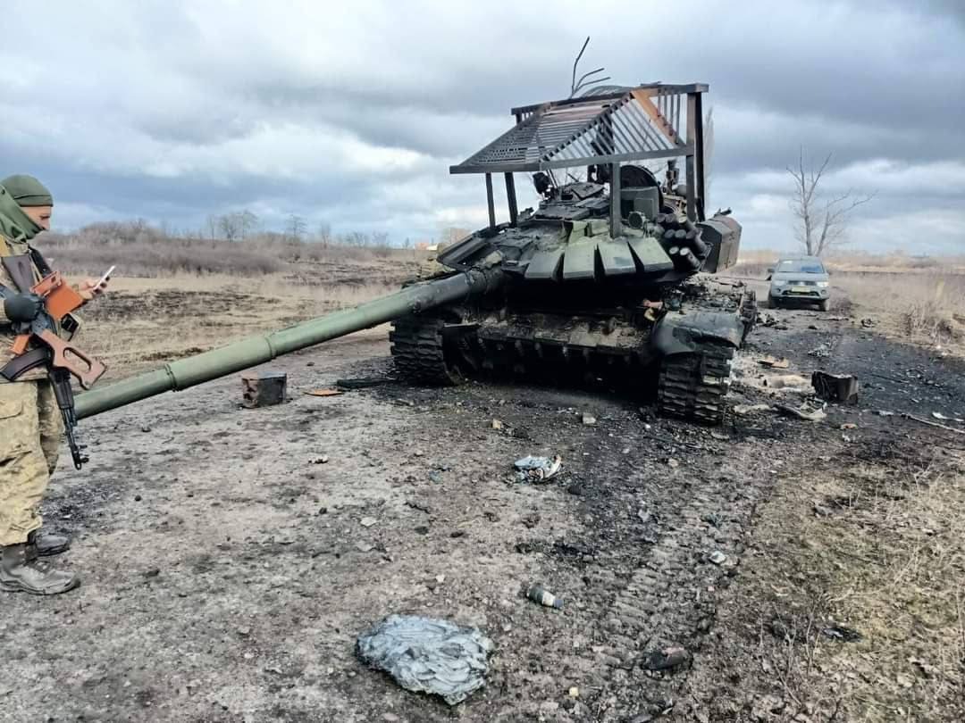 טנק רוסי מושמד אשר צוייד ב-"מיגון גג" ולידו חייל אוקראיני מרוצה.